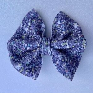 May include: A large, handmade hair bow in a classic bow shape. The bow is made of a soft, textured fabric in a dark blue color, with a pattern of small, colorful dots. The bow is a stylish accessory.