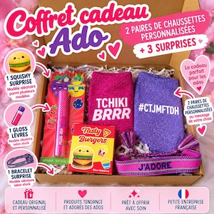 Pode incluir: Uma caixa de presente contendo dois pares de meias brilhantes em rosa e roxo com o texto TCHIKI BRRR e #CTJMFTDH, um brilho labial rosa, um brinquedo squishy Tasty Burgers e uma pulseira tecida com o texto J'ADORE.