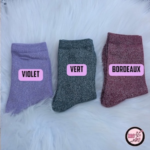 May include: Three pairs of sparkly socks in violet, green, and burgundy. Each sock has a rectangular label with the color name in white text. The socks are displayed on a white, fluffy surface.