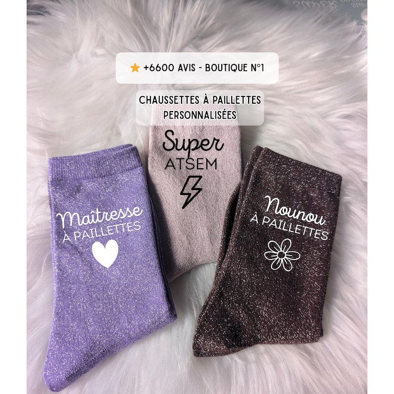 May include: Three pairs of sparkly socks in lavender, taupe, and brown. The lavender sock has a white heart and the words "Ma&icirc;tresse &Agrave; PAILLETTES". The taupe sock has a lightning bolt and the word "Super ATSEM". The brown sock has a flower and the words "Nounou &Agrave; PAILLETTES".
