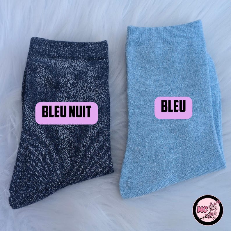 May include: Two pairs of socks, one navy blue and one light blue, are displayed on a white surface. Each sock has a pink rectangle with the word "BLEU" or "BLEU NUIT" printed on it. The socks are made of a soft, textured material.