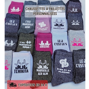 Peut inclure: Une collection de chaussettes à paillettes personnalisées de différentes couleurs, chacune avec du texte et des graphiques blancs uniques. Les chaussettes affichent des phrases comme "C'est Marseille Bébé" et "Le J C'est Les". Le texte "EXPEDITION EN 24 H" est également présent.