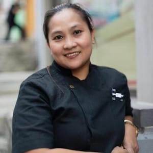 Op de afbeelding: Een vrouw die een zwart koksuniform draagt met een wit logo met de tekst "The Butcher's Club" op de linker borst.