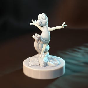 May include: A 3D-printed figurine of a cartoon lizard in a playful pose, standing on a rock formation atop a circular base. The lizard is light gray, with its arms outstretched and one leg raised. The base and rock are also light gray.