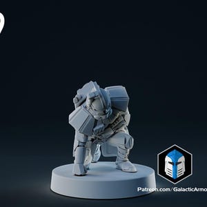 Op de afbeelding: Een lichtgrijze miniatuurfiguur van een futuristische gepantserde soldaat in een hurkende positie. De figuur staat op een cirkelvormige basis. Het nummer "9" staat in de linkerbovenhoek. Het logo en de website van Galactic Armory staan rechtsonder.