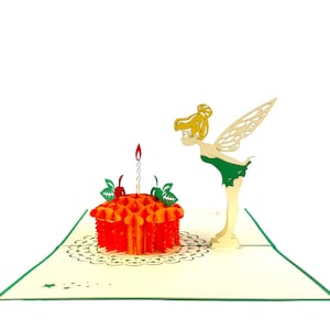 May include: A 3D pop-up card featuring a fairy with green wings and a dress looking at a birthday cake with a single lit candle. The cake is orange and has green leaves and red cherries on top. The card is on a cream background with a green and white lace design.