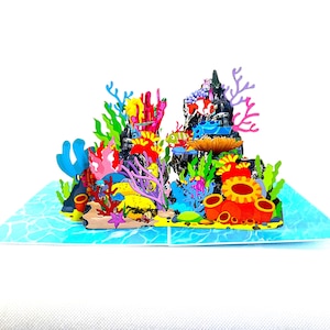Pode incluir: Um cartão pop-up colorido com uma cena de recife de coral subaquático. O cartão apresenta corais vibrantes, peixes e outras criaturas marinhas em tons de vermelho, amarelo, azul e verde. O cartão está aberto, revelando o design 3D.