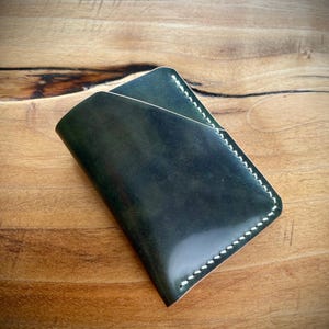 May include: A dark green leather wallet with white stitching. The wallet is folded in half and has a smooth, textured surface.