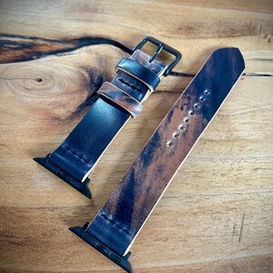 May include: Two black leather Apple Watch bands with a distressed, brown and blue pattern. One band has a black buckle.