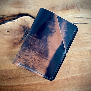 May include: A black and brown leather wallet with a distressed finish. The wallet has a stitched edge and a folded design.