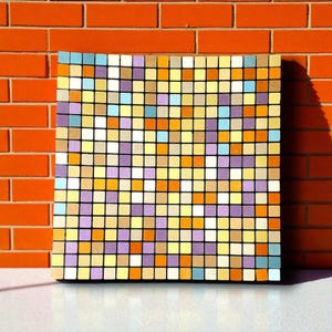 Può includere: Un'opera d'arte quadrata in legno con un design a mosaico. Il mosaico è composto da piccoli quadrati colorati nelle tonalità di giallo, arancione, viola, blu e beige. L'opera è esposta contro un muro di mattoni rossi.