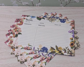 May include: A stack of floral recipe cards with a white background and a floral border. The cards have lines for writing down ingredients, directions, and oven temperature. The text "RECIPE" is printed at the top of the card.