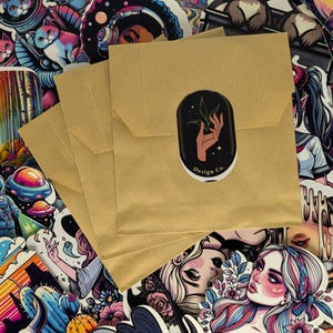 Puede incluir: Un conjunto de sobres de papel marrón con una pegatina en la parte delantera. La pegatina es en blanco y negro y presenta una mano sosteniendo una pequeña planta. El texto en la pegatina dice "Design Co."