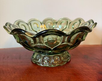 May include: A translucent forest green glass bowl featuring a repeating moon and star pattern along the exterior. The bowl has a scalloped, ruffled rim and sits on a circular pedestal base decorated with a matching star motif in the glass.