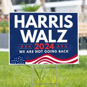 May include: A blue and red political yard sign with the text "HARRIS WALZ 2024 WE ARE NOT GOING BACK" and a stylized American flag design.