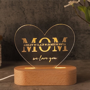 May include: A heart-shaped LED night light with the word "MOM" and the names Ashley, Clair, James, and Sofia. The light is on a wooden base and says "we love you".
