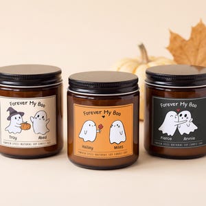 May include: Three amber glass jar candles with black lids, each featuring a label with the text Forever My Boo and Pumpkin Spice Natural Soy Candle. The labels display cartoon ghost illustrations with names Troy, Abed, Hailey, Miles, Pierce, and Annie.