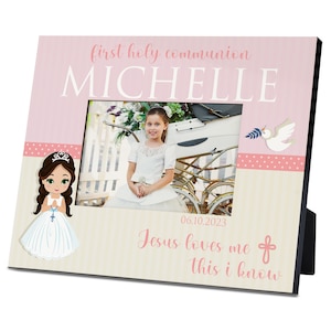 May include: A pink and white photo frame with a picture of a young girl in a white dress. The frame has a pink polka dot border and the text "first holy communion" and "MICHELLE" in white. The date "06.10.2023" and the text "Jesus loves me this I know" are also on the frame.