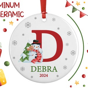 May include: A 3 inch round white ceramic or aluminum ornament with a red letter D, a snowman holding a "Merry Christmas" sign, and the name Debra and the year 2024.