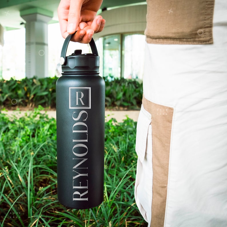 K&ouml;nnte beinhalten: Eine schwarze Edelstahl-Wasserflasche mit Henkel und einer silbernen Aufschrift "R REYNOLDS".