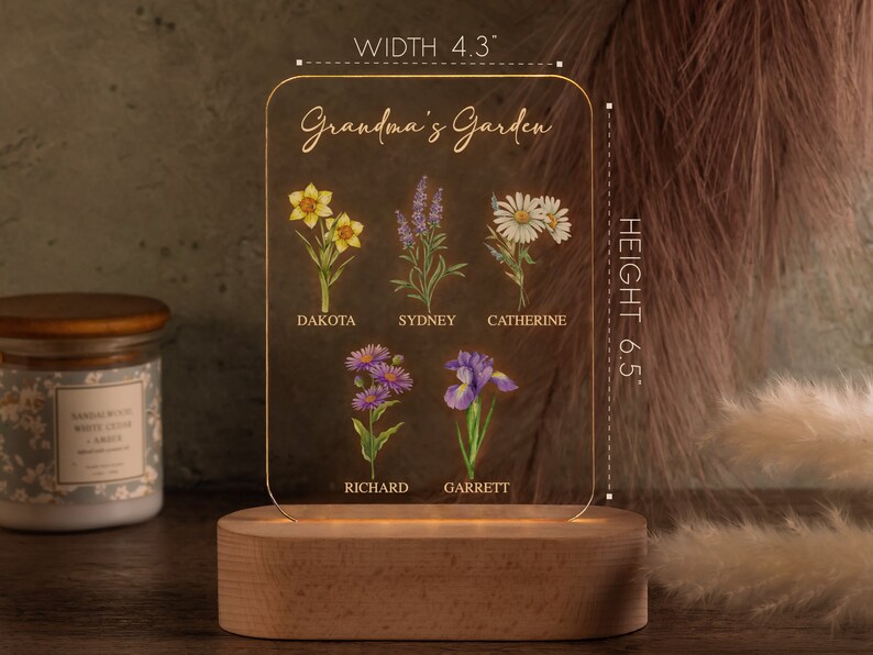 May include: A personalized acrylic garden sign with a wooden base. The sign features the text "Grandma's Garden" and illustrations of various flowers, with names like Dakota, Sydney, and Catherine. The sign is 4.3 inches wide and 6.5 inches tall.