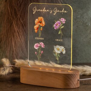 May include: A personalized acrylic night light with a wooden base. The clear acrylic panel features the text "Grandma's Garden" and watercolor illustrations of flowers with names below. The base is made of wood and has a warm glow.