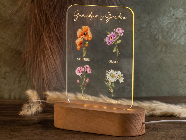 May include: A personalized acrylic night light with a wooden base. The clear acrylic panel features the text "Grandma's Garden" and watercolor illustrations of flowers with names below. The base is made of wood and has a warm glow.