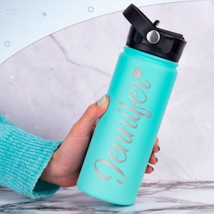K&ouml;nnte beinhalten: Eine t&uuml;rkisfarbene Wasserflasche mit schwarzem Deckel und einer silbernen Aufschrift "Jennifer" mit einem kleinen Herzsymbol.