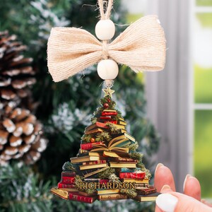 May include: A Christmas tree ornament shaped like a stack of books with a bow and beads hanging from the top. The ornament is personalized with the name "RICHARDSON".