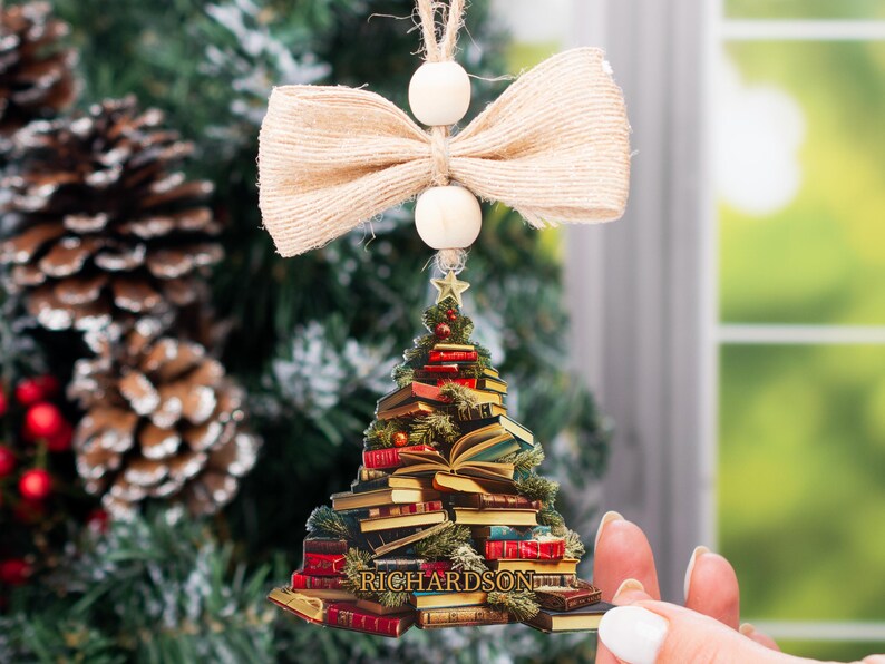 May include: A Christmas tree ornament shaped like a stack of books with a bow and beads hanging from the top. The ornament is personalized with the name "RICHARDSON".