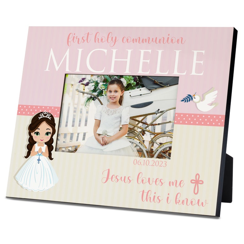 May include: A pink and white photo frame with a picture of a young girl in a white dress. The frame has a pink polka dot border and the text "first holy communion" and "MICHELLE" in white. The date "06.10.2023" and the text "Jesus loves me this I know" are also on the frame.