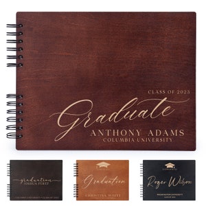 May include: A brown wooden photo album with a gold inscription that reads "Class of 2023 Graduate Anthony Adams Columbia University". The album has a spiral binding and is closed.