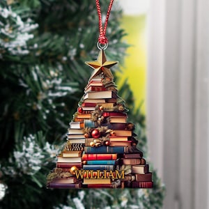 May include: A Christmas tree ornament shaped like a stack of books with a gold star on top. The ornament is decorated with red and green ornaments and the name "WILLIAM" is printed at the bottom.