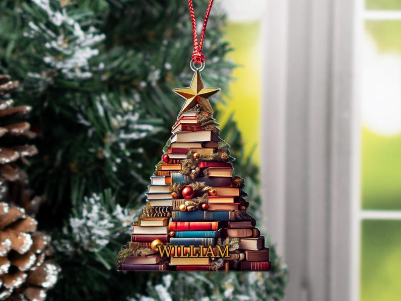 May include: A Christmas tree ornament shaped like a stack of books with a gold star on top. The ornament is decorated with red and green ornaments and the name "WILLIAM" is printed at the bottom.