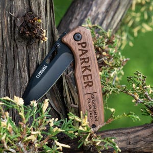 May include: A black pocket knife with a wooden handle engraved with the name "Parker" and the text "Groomsman 09.09.2025".