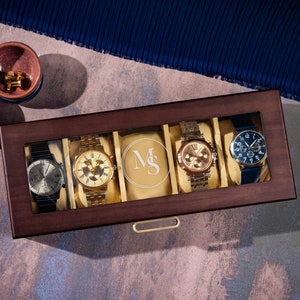 May include: A wooden watch box with a glass top, displaying five watches. The box has a drawer and is engraved with the initials "M&S".