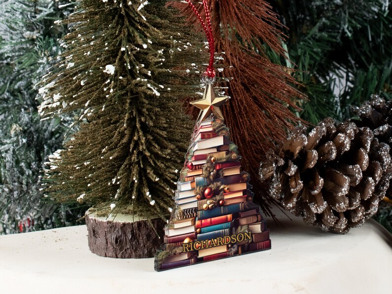 May include: A Christmas tree ornament shaped like a stack of books with a gold star on top. The ornament is decorated with red and green ornaments and has the word "RICHARDSON" at the bottom.