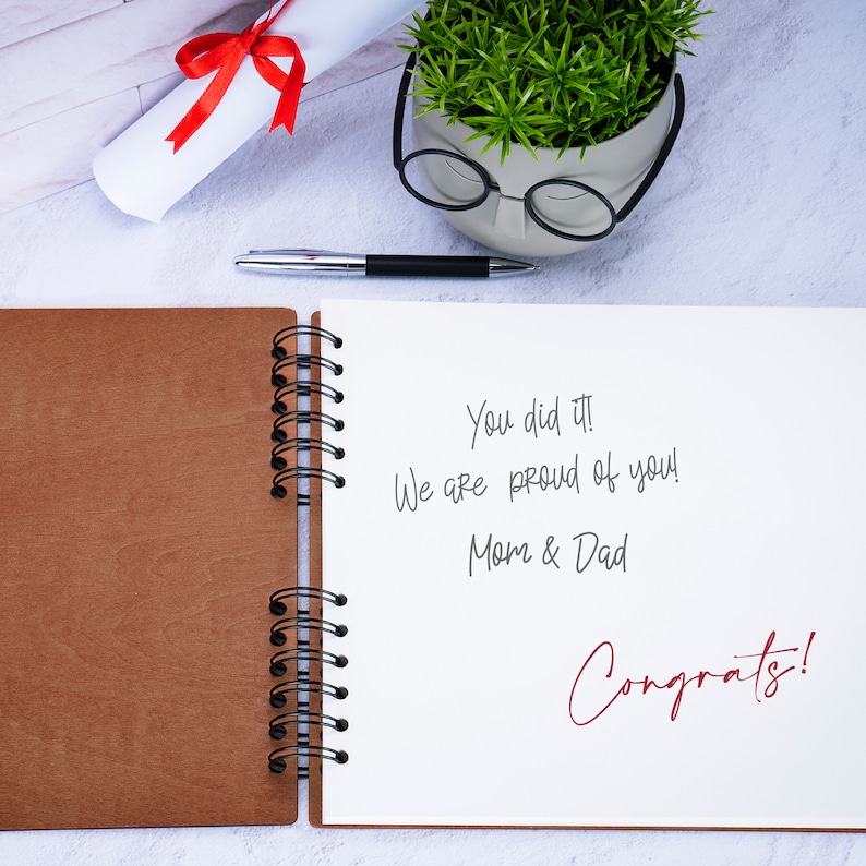 May include: An open brown leather bound journal with a white page showing a handwritten message that says "You did it! We are proud of you! Mom & Dad Congrats!"