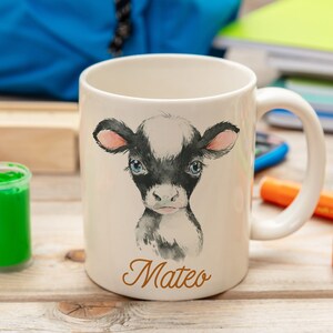 May include: White ceramic mug with a black and white watercolor illustration of a calf. The mug has a black handle and the name "Mateo" is written in brown cursive on the bottom.