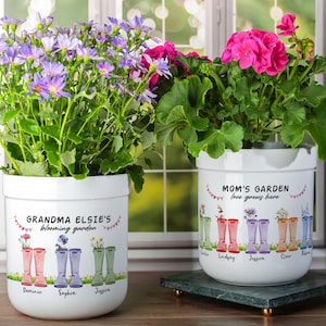 May include: Two white ceramic flower pots with colorful rain boots and floral designs. The text on the pots reads "Grandma Elsie's blooming garden" and "Mom's Garden love grows here".