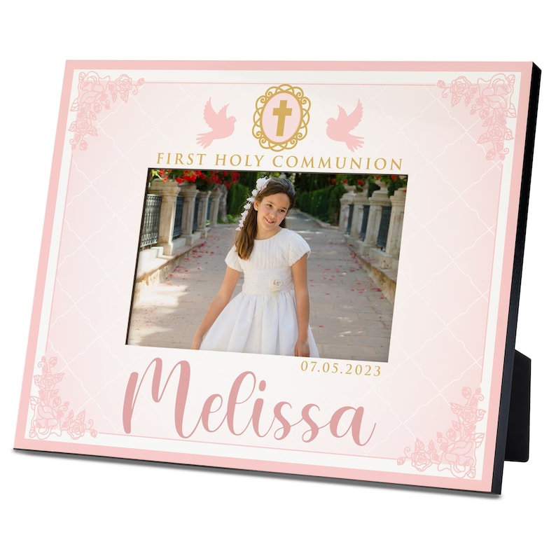 May include: A pink picture frame with a white mat and a gold cross design. The frame has a photo of a girl in a white dress and the text "First Holy Communion" and "Melissa 07.05.2023".