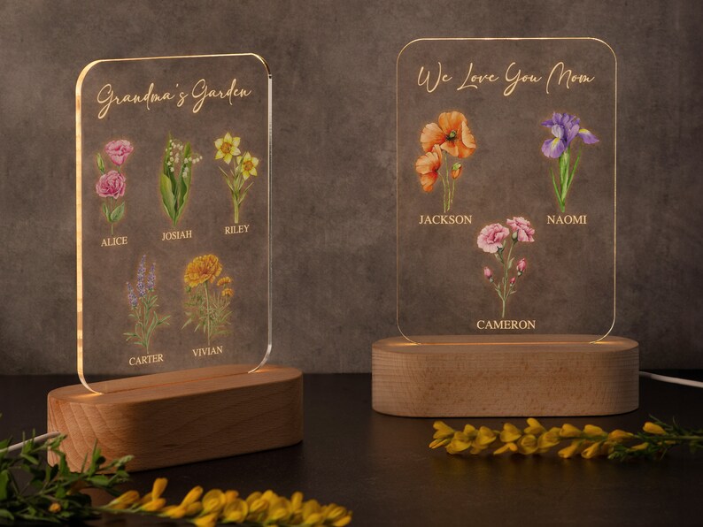 May include: Two illuminated acrylic plaques with wooden bases. One reads "Grandma's Garden" with floral illustrations and names. The other says "We Love You Mom" with flowers and names. Both are lit with a warm glow.