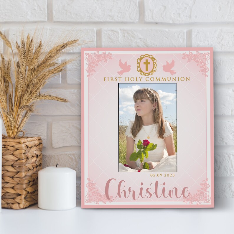May include: Pink photo frame with a white border and a gold cross design. The frame has a photo of a girl holding a red rose. The text "First Holy Communion" and "Christine" are printed on the frame. The date "05.09.2023" is also printed on the frame.