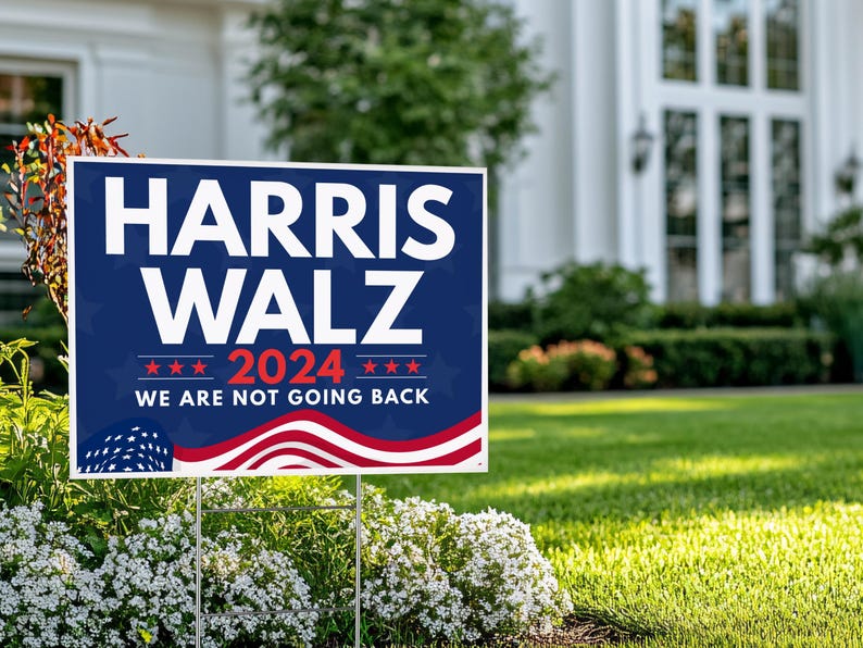 May include: A blue and red political yard sign with the text "HARRIS WALZ 2024 WE ARE NOT GOING BACK" and a stylized American flag design.