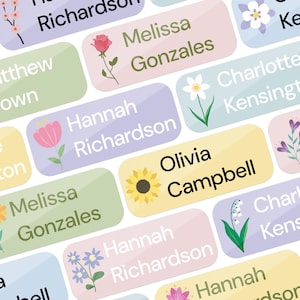 May include: A collection of pastel-colored name labels with floral illustrations. Each label features a name in a white font, with flowers like roses, sunflowers, and tulips. The labels are rectangular with rounded corners.