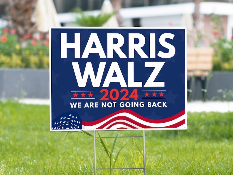 May include: A blue and red political yard sign with the text "HARRIS WALZ 2024 WE ARE NOT GOING BACK" and a stylized American flag design.
