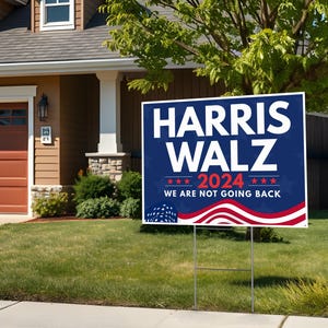 May include: A blue and red political yard sign with the text "HARRIS WALZ 2024 WE ARE NOT GOING BACK" and a stylized American flag design.