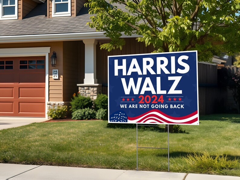 May include: A blue and red political yard sign with the text "HARRIS WALZ 2024 WE ARE NOT GOING BACK" and a stylized American flag design.