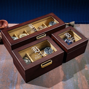 May include: Three wooden watch boxes with glass lids. The boxes are brown and have a gold-colored latch. The boxes are personalized with the letter "B" and the name "Brown".