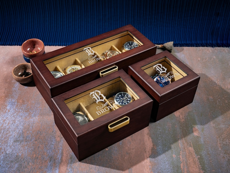 May include: Three wooden watch boxes with glass lids. The boxes are brown and have a gold-colored latch. The boxes are personalized with the letter "B" and the name "Brown".